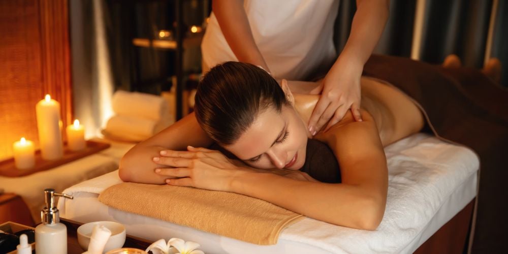Woman receiving a relaxing back and shoulder massage from a therapist in a warm, candlelit spa.